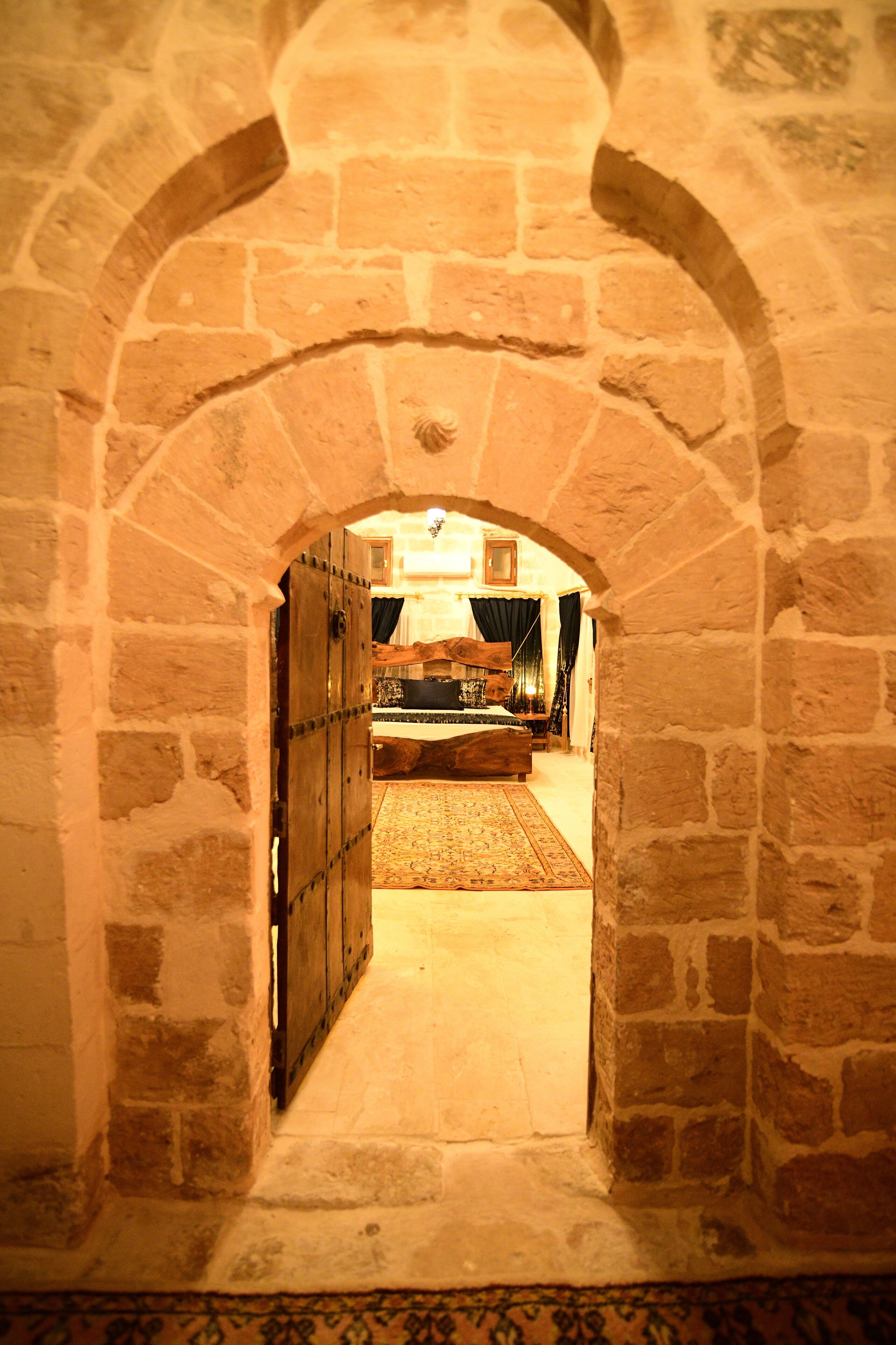 An arched stone corridor leading to a bedroom with a bed, a nightstand, and a dresser.