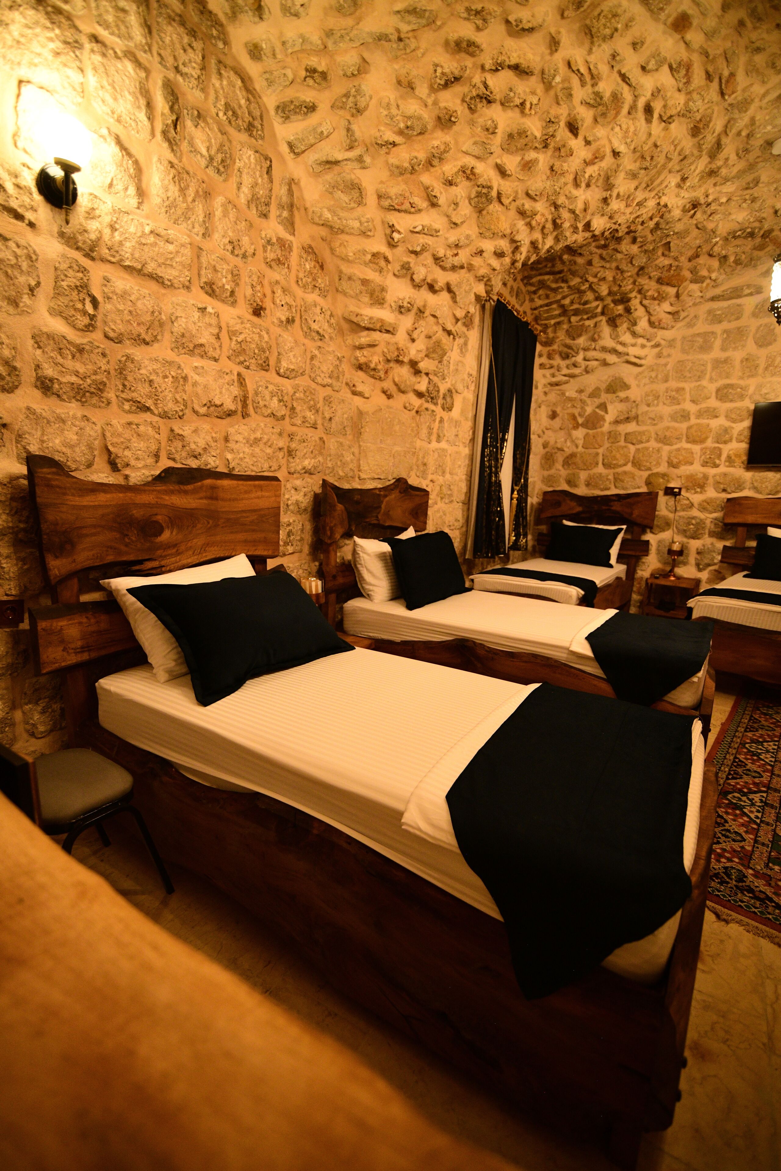 Habitación con paredes de piedra y cuatro camas, cada una con cabeceros de madera y ropa de cama negra.