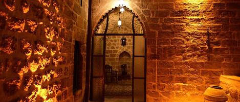 Un edificio de piedra con un arco de entrada, una mesa pequeña y una olla grande.