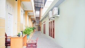 A corridor with a reception desk, chairs, potted plants, and air conditioning units. - Hotel O Tanjung Karang Near Central Plaza Formerly Wisma Bambu (Bandar Lampung)