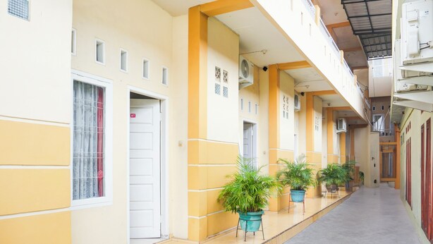 A corridor with doors, potted plants, and a tiled floor. - Hotel O Tanjung Karang Near Central Plaza Formerly Wisma Bambu (Bandar Lampung)