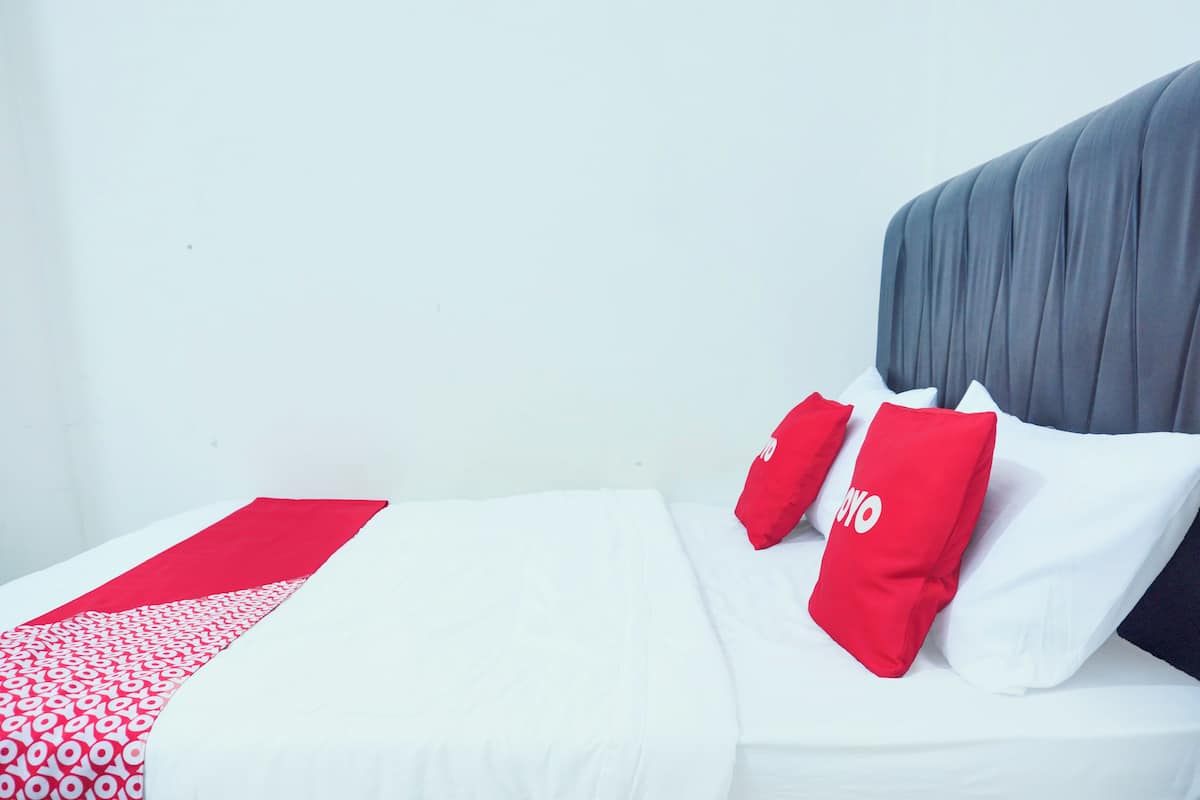 Una cama con ropa blanca y almohadas rojas y blancas, cabecera gris y una alfombra roja y blanca estampada.