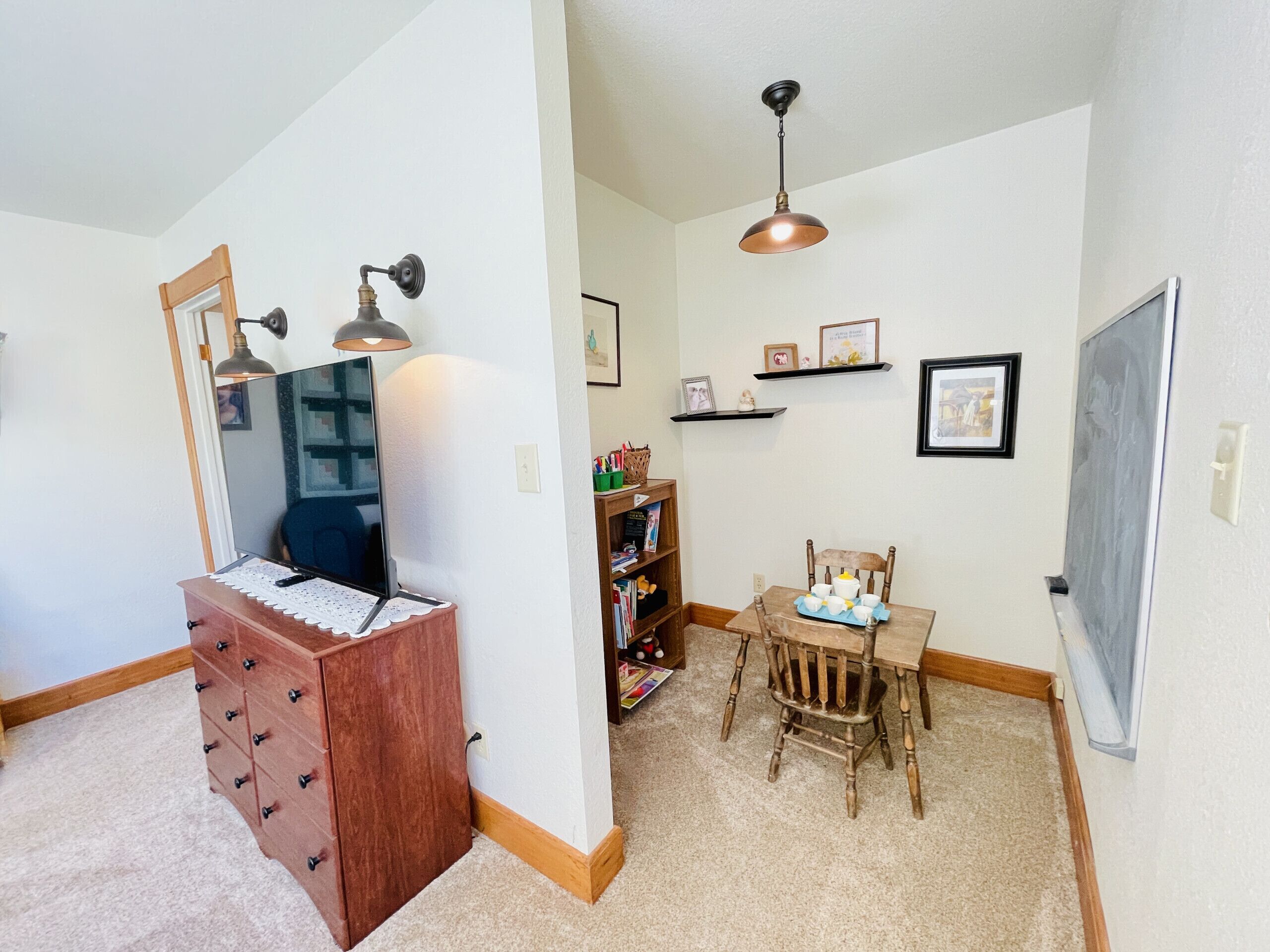 A room with a wooden dresser, a desk with a computer, a chair, a bookshelf, and a ceiling light fixture.