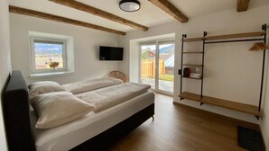 A bedroom with a bed, a TV, a window with a view, and a wooden ceiling. - Large Saalfelden Apartment With Terrace (Saalfelden am Steinernen Meer)