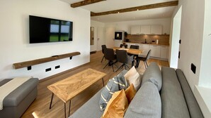 A modern living room with a sofa, a wooden coffee table, and a TV mounted on the wall. - Large Saalfelden Apartment With Terrace (Saalfelden am Steinernen Meer)