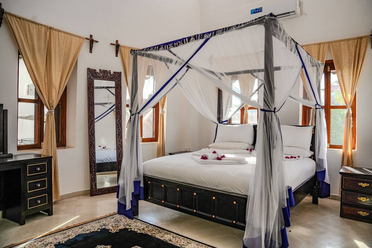 A four-poster bed with a canopy, a large mirror, and a wooden dresser.