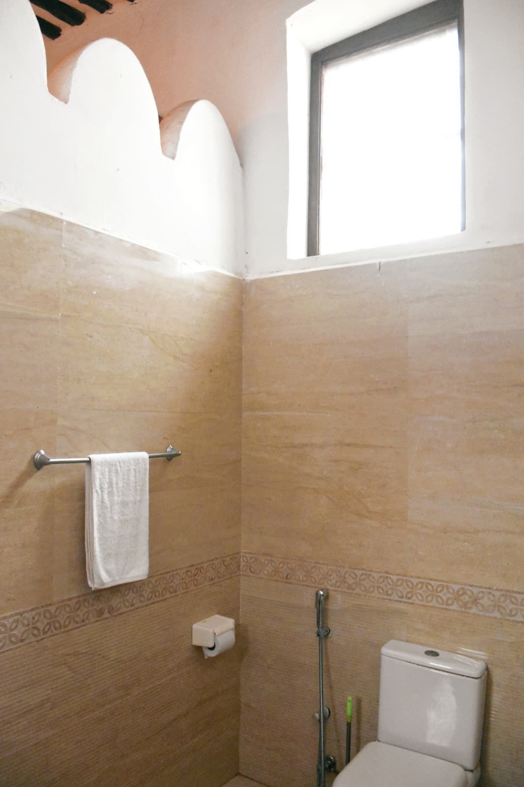 A bathroom with a shower, toilet, towel rack, and a window.