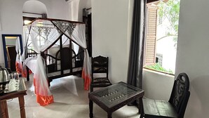 A room with a bed, a table, and a chair. There is a window with curtains and a view of the outside.