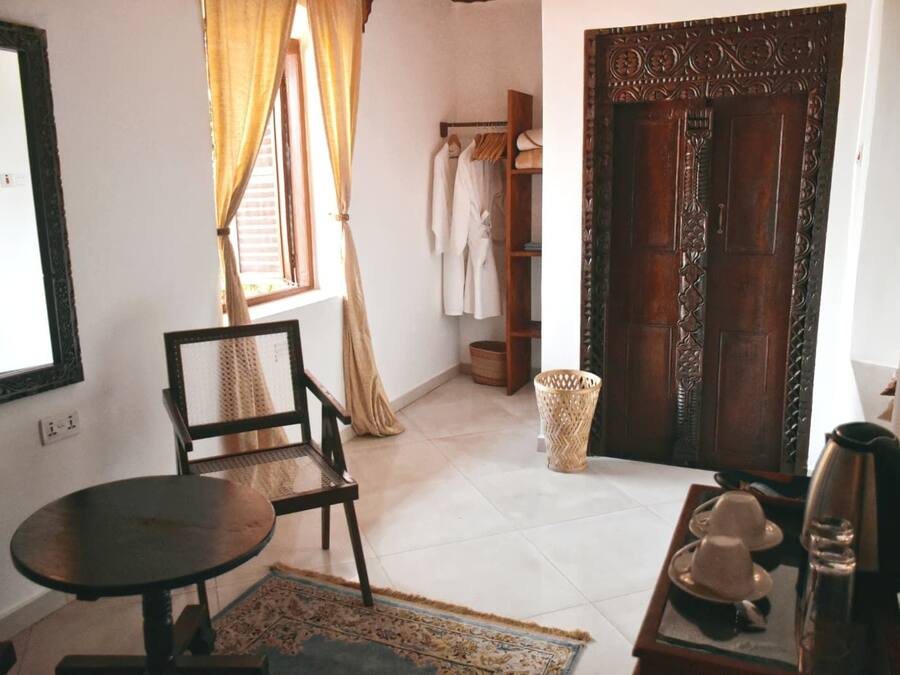A room with a wooden door, a chair, a small table, a basket, and a window with curtains.