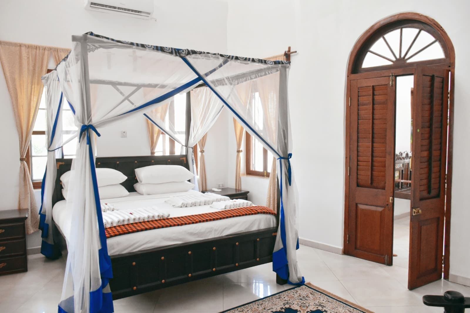 A four-poster bed with a canopy, a wooden door, and a tiled floor.
