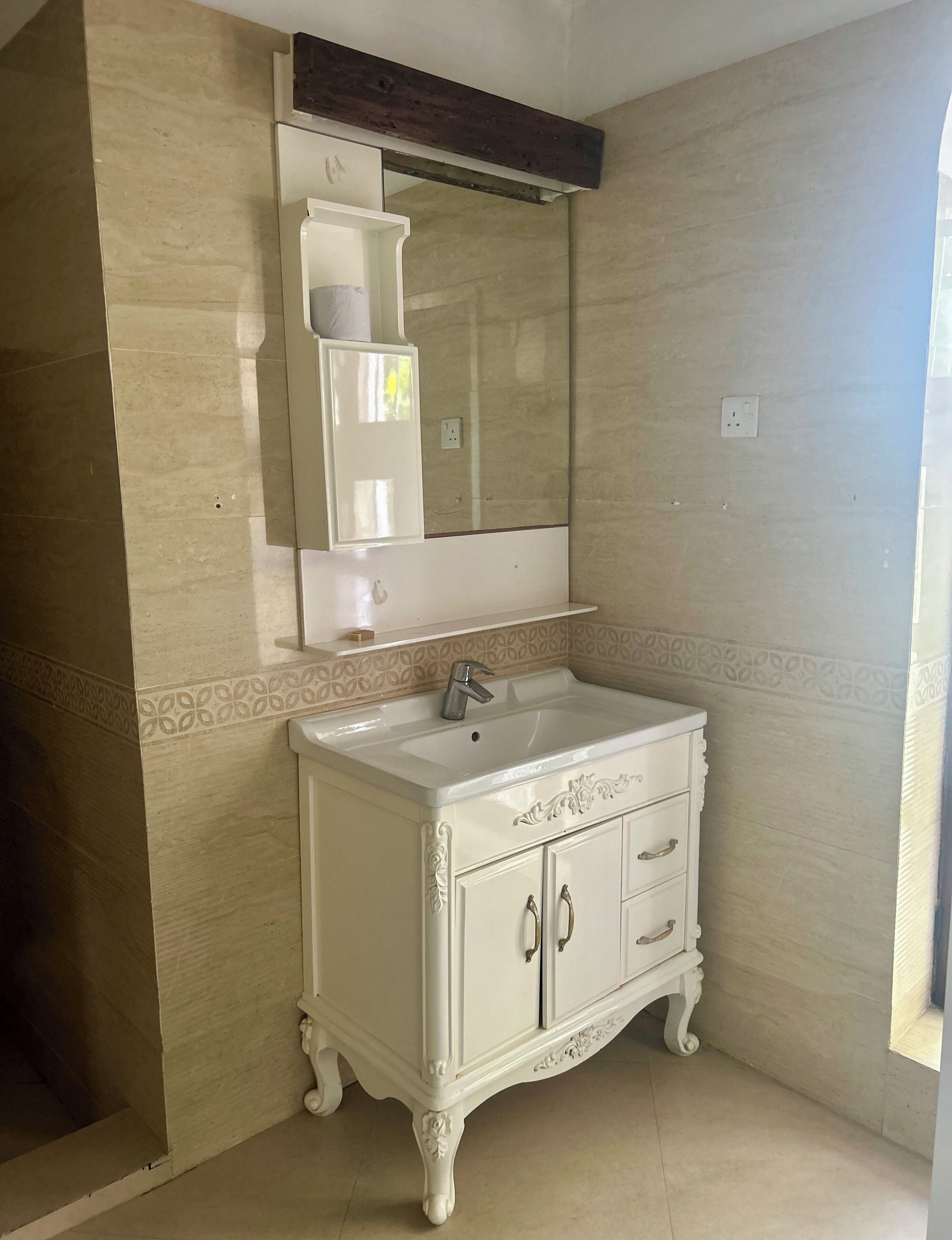 Un baño con tocador blanco, espejo y paredes cubiertas de azulejos color beige.