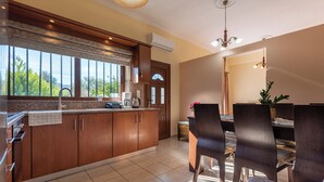A modern kitchen with wooden cabinets, a dining area with dark chairs, and a large window with a view of greenery.