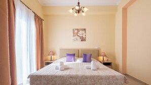 A double bed with a floral bedspread, two purple pillows, and two white towels. There are two bedside tables with lamps and a painting on the wall above the bed.