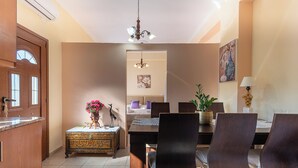A dining area with a wooden table, dark chairs, a chandelier, and a potted plant.