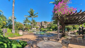 Un área de piscina en un resort con sillones de descanso, una pérgola y palmeras.