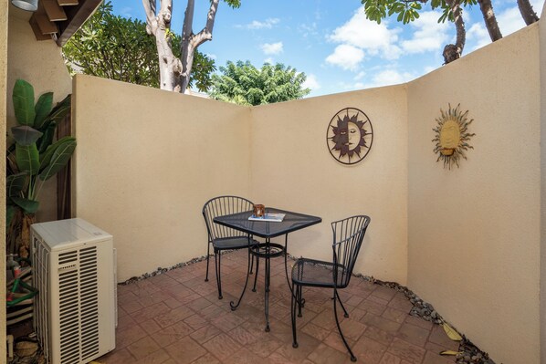 A patio with a table and chairs, an air conditioning unit, and decorative wall art.