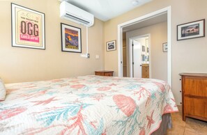 A bedroom with a floral bedspread, a framed OGG poster, and a wooden nightstand.
