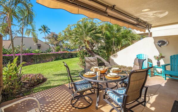Un patio al aire libre con una mesa redonda dispuesta para comer, rodeada de sillas, y un área techada con ventilador de techo.