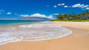 Una playa con aguas turquesas cristalinas, una orilla arenosa y una montaña al fondo.