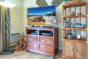 A living room with a television displaying a beach scene, a wooden cabinet with decorative items, and a wicker side table.