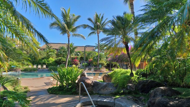 Zona de piscina en un resort, con una pequeña fuente, palmeras y sillones de descanso.