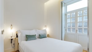 Ein Schlafzimmer mit einem großen Bett, zwei Nachttischen, einem Beistelltisch und einem Fenster mit satinierten Glasscheiben.