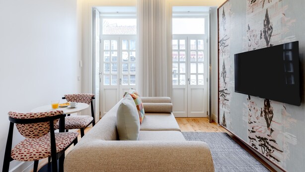 Een moderne woonkamer met een bank, stoelen, een klein tafeltje met een glas sinaasappelsap en een aan de muur bevestigde televisie.