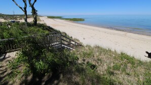 Ein Strand mit einer Holztreppe, die zum Ufer führt, umgeben von viel Grün und blauem Himmel.