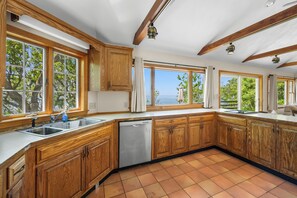 A kitchen with wooden cabinets, a dishwasher, and large windows with curtains. - Beachfront Home Offering Direct Access to Your Own Private Beach (2386) (Brewster)