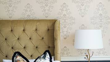 A bedroom with a tufted headboard, a framed painting, a decorative lamp, and a patterned wall.