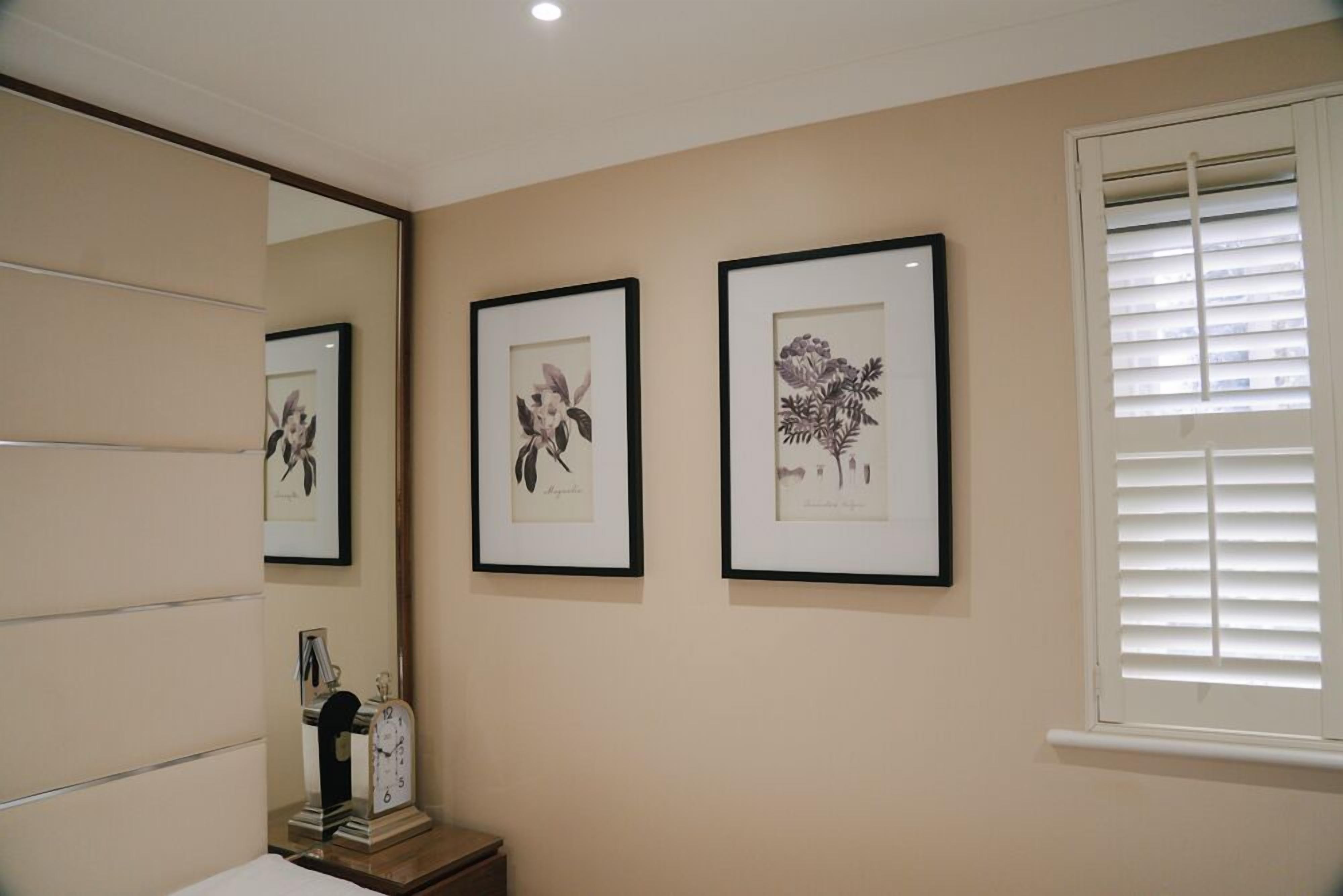 A bathroom with a mirror, a clock, and three framed botanical prints on the wall.