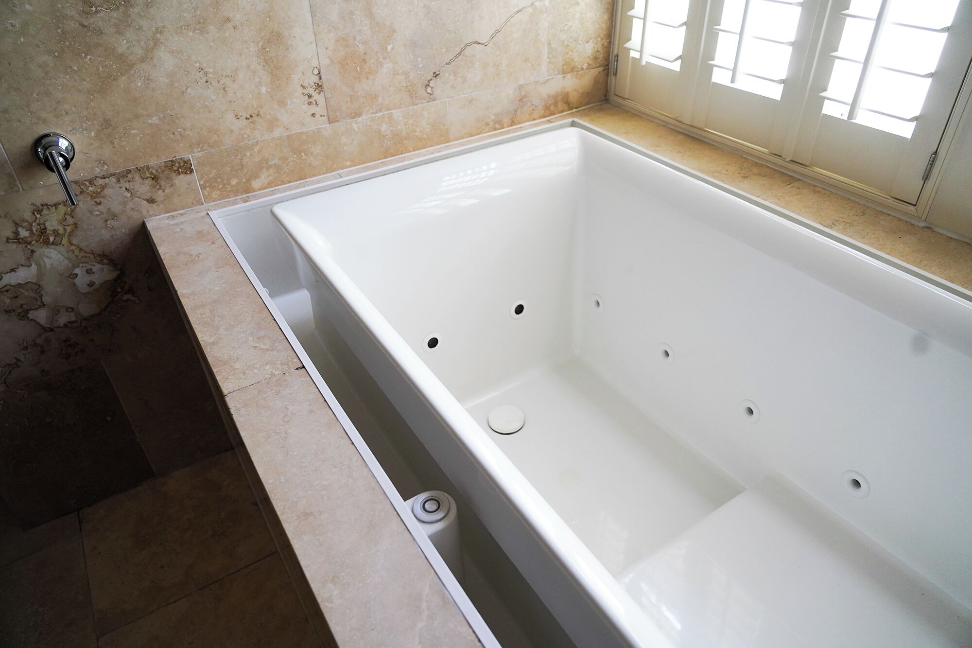 A large, empty bathtub in a bathroom with tiled walls and a window.