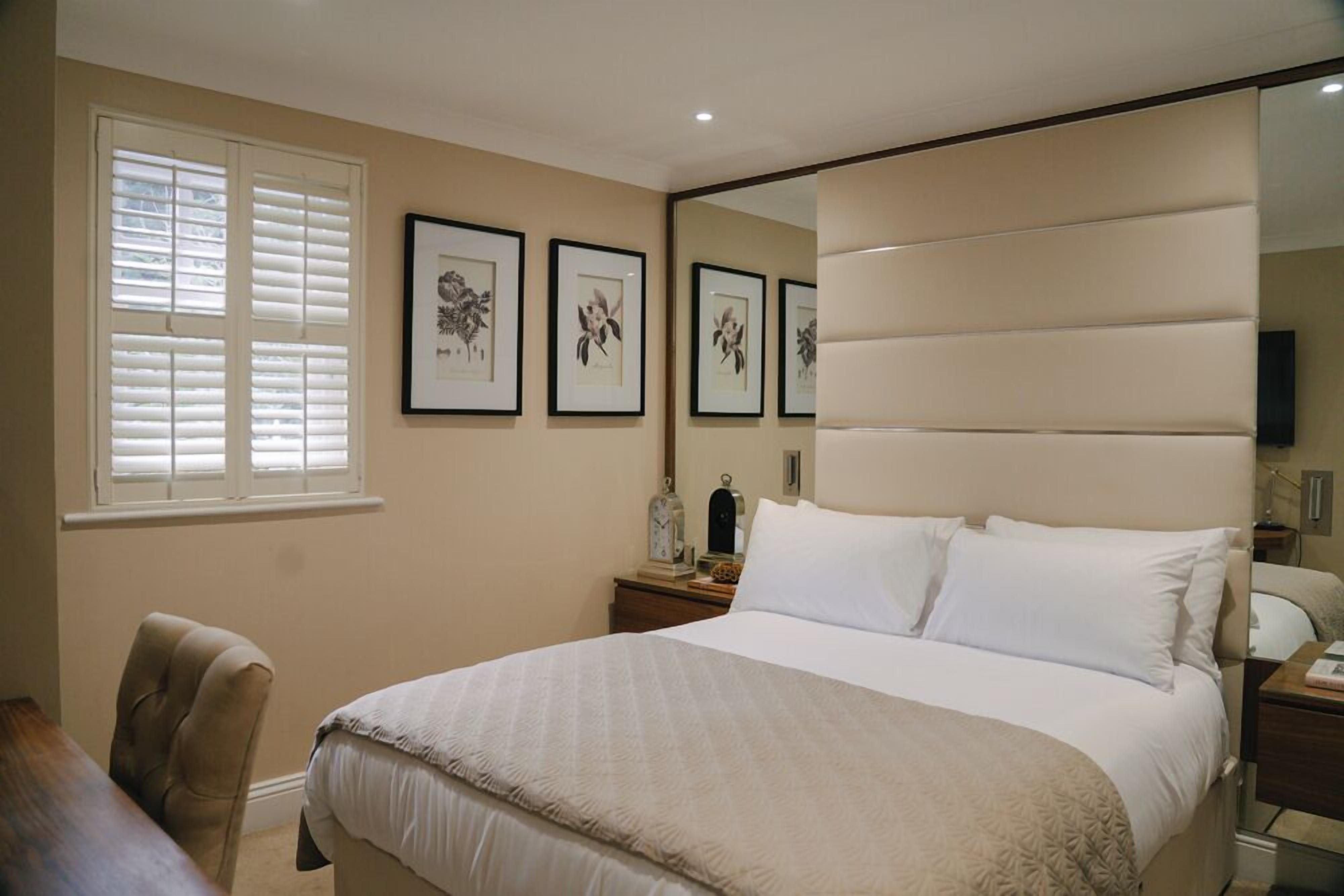 A bedroom with a large bed, a chair, a nightstand, a mirror, and framed botanical prints on the wall.