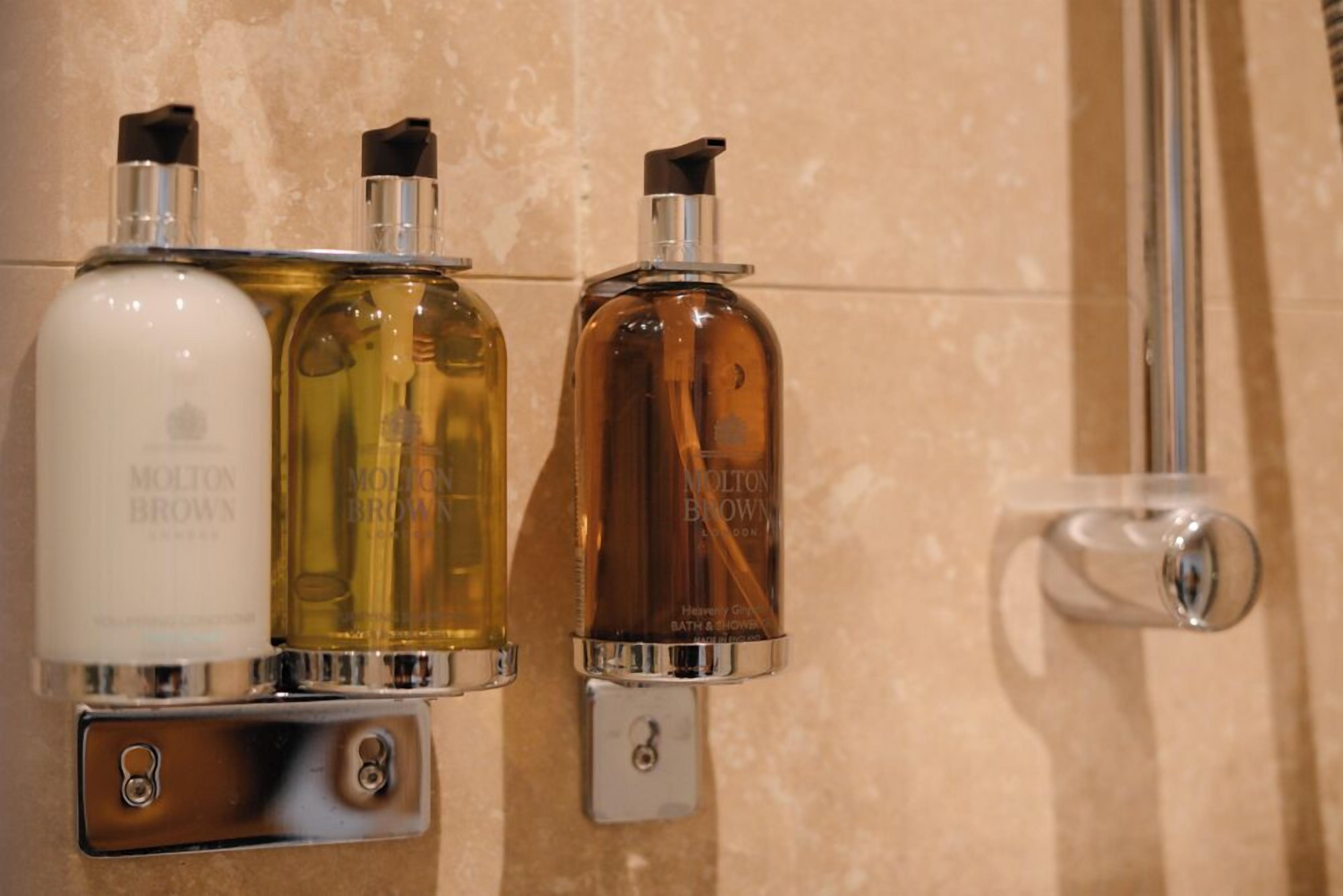 Three bathroom dispensers with different colored liquids, mounted on a wall with a metallic handle.