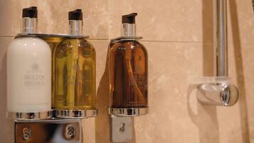 Three bathroom dispensers with different colored liquids, mounted on a wall with a metallic handle.