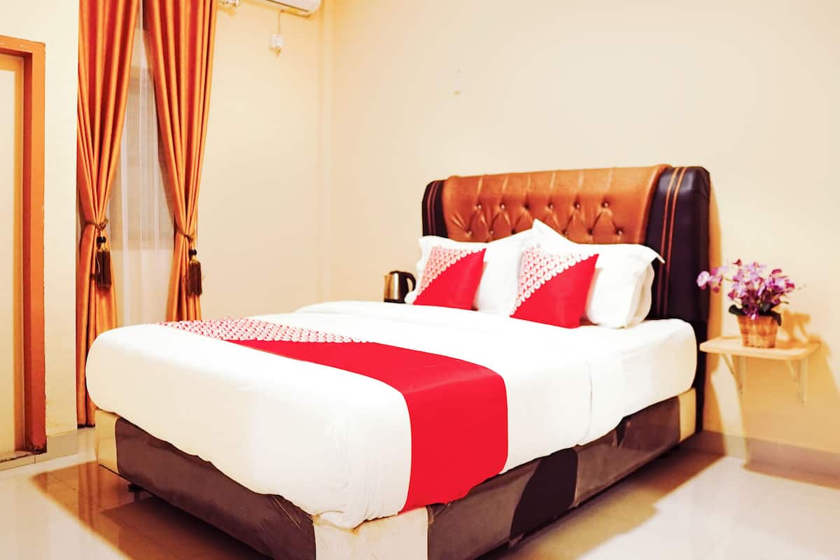 A neatly made bed with a red and white bedspread, a tufted headboard, and a small bedside table with a vase of flowers.