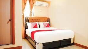 Una cama bien hecha con una colcha roja y blanca, un cabecero de madera y una ventana con cortinas.