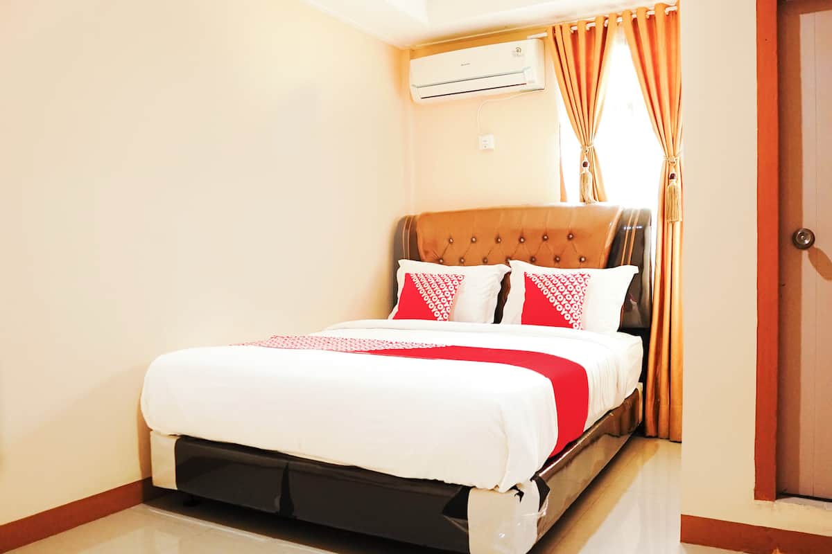 A neatly made bed with a red and white bedspread, a brown upholstered headboard, and a white air conditioning unit above it.