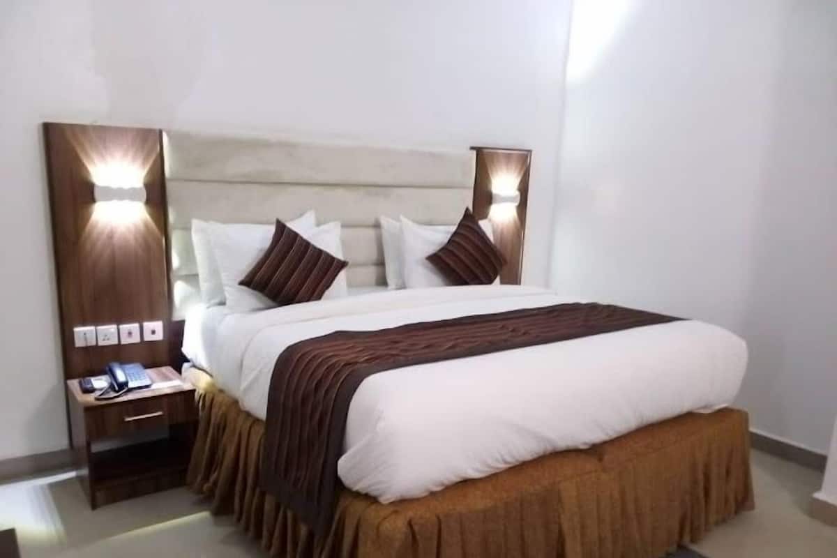 Une chambre d’hôtel avec un grand lit, une table de chevet avec un téléphone et des lampes fixées au mur.