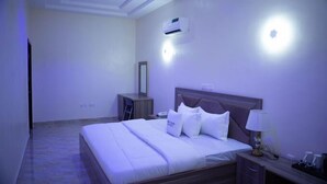 A hotel room with a bed, bedside table, lamp, and an air conditioning unit on the wall. - Mamma Chare Hotel  (Jimeta)