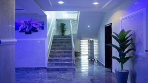 A hallway with marble flooring, a staircase, a potted plant, and a tiger mural on the wall. - Mamma Chare Hotel  (Jimeta)