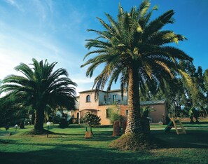 A building with a tiled roof, surrounded by palm trees and a well-maintained lawn. - Classical Residence Baia Delle Palme 2 Bedroom Apartment Sleeps 6 Persons T6 (Pula)