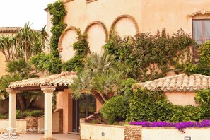 A building with arched windows and a tiled roof, surrounded by lush greenery and flowering plants. - Classical Residence Baia Delle Palme 2 Bedroom Apartment Sleeps 6 Persons T6 (Pula)