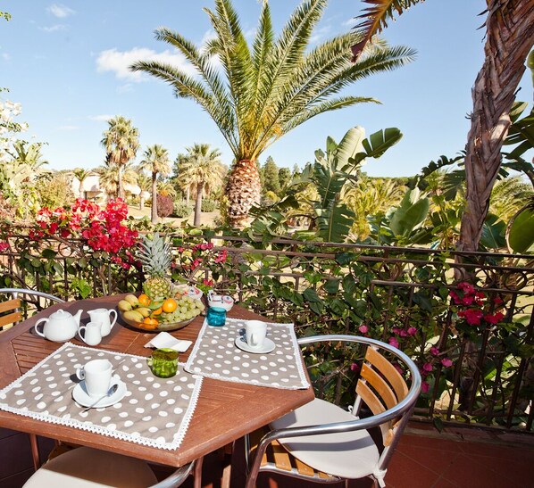 An outdoor dining area with a table set for two, surrounded by lush greenery and a variety of tropical plants. - Classical Residence Baia Delle Palme 2 Bedroom Apartment Sleeps 6 Persons T6 (Pula)