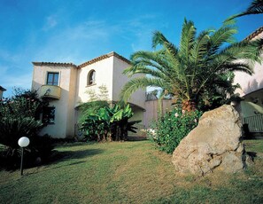 A two-story building with a tiled roof, surrounded by lush greenery and a large rock. - Classical Residence Baia Delle Palme 2 Bedroom Apartment Sleeps 6 Persons T6 (Pula)