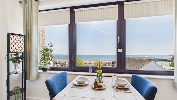 Ein Esstisch mit Blick auf das Meer und den Strand, eine Topfpflanze und eine dekorative Vase.