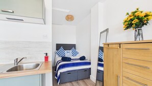 Ein gemütliches Hotelzimmer mit Küchenzeile, einem Bett mit gestreifter Bettwäsche, einem Holzschrank und einer Vase mit gelben Blumen.