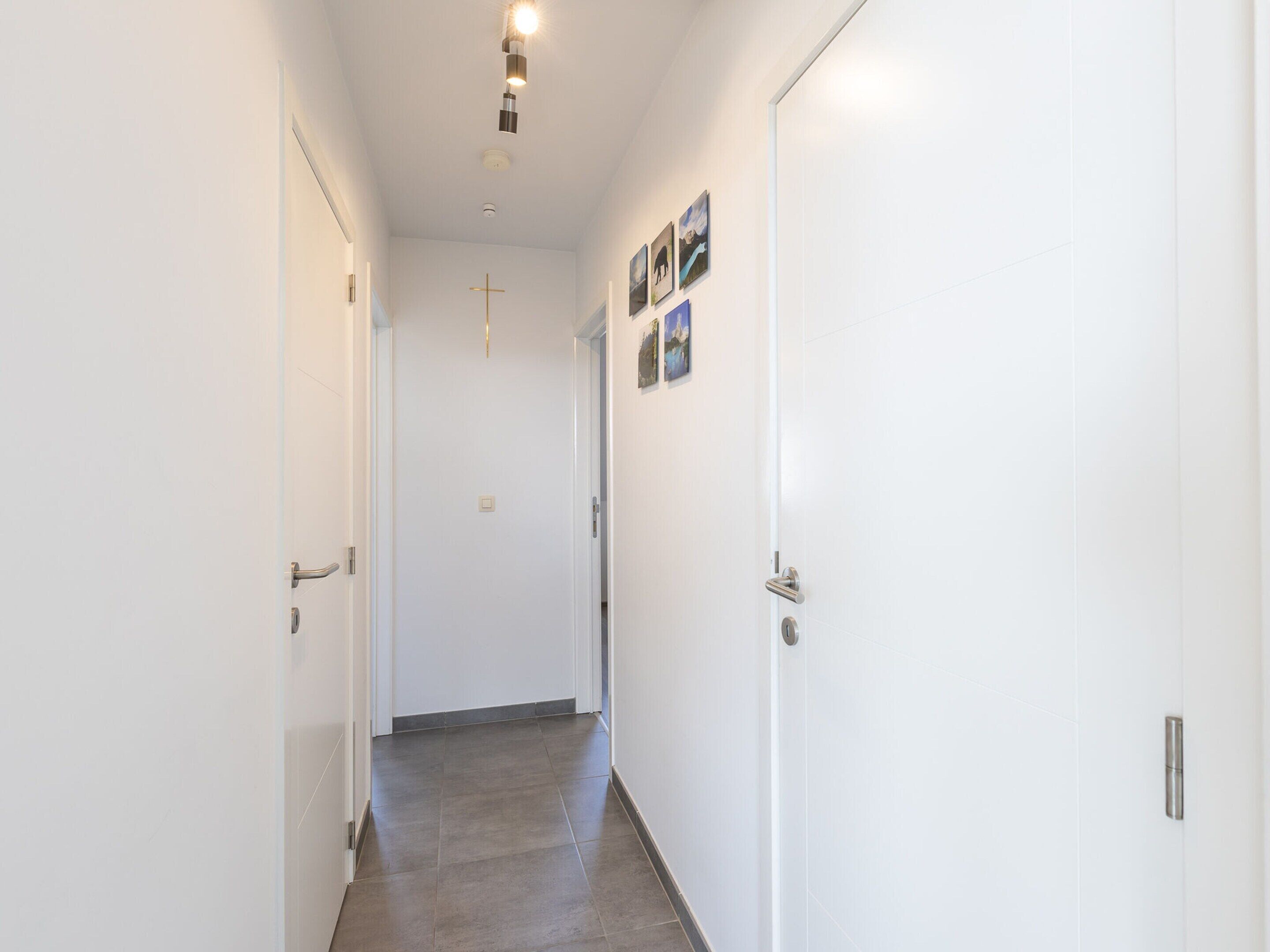 Un corridoio stretto con pareti e porte bianche, pavimento piastrellato e una lampada a soffitto.