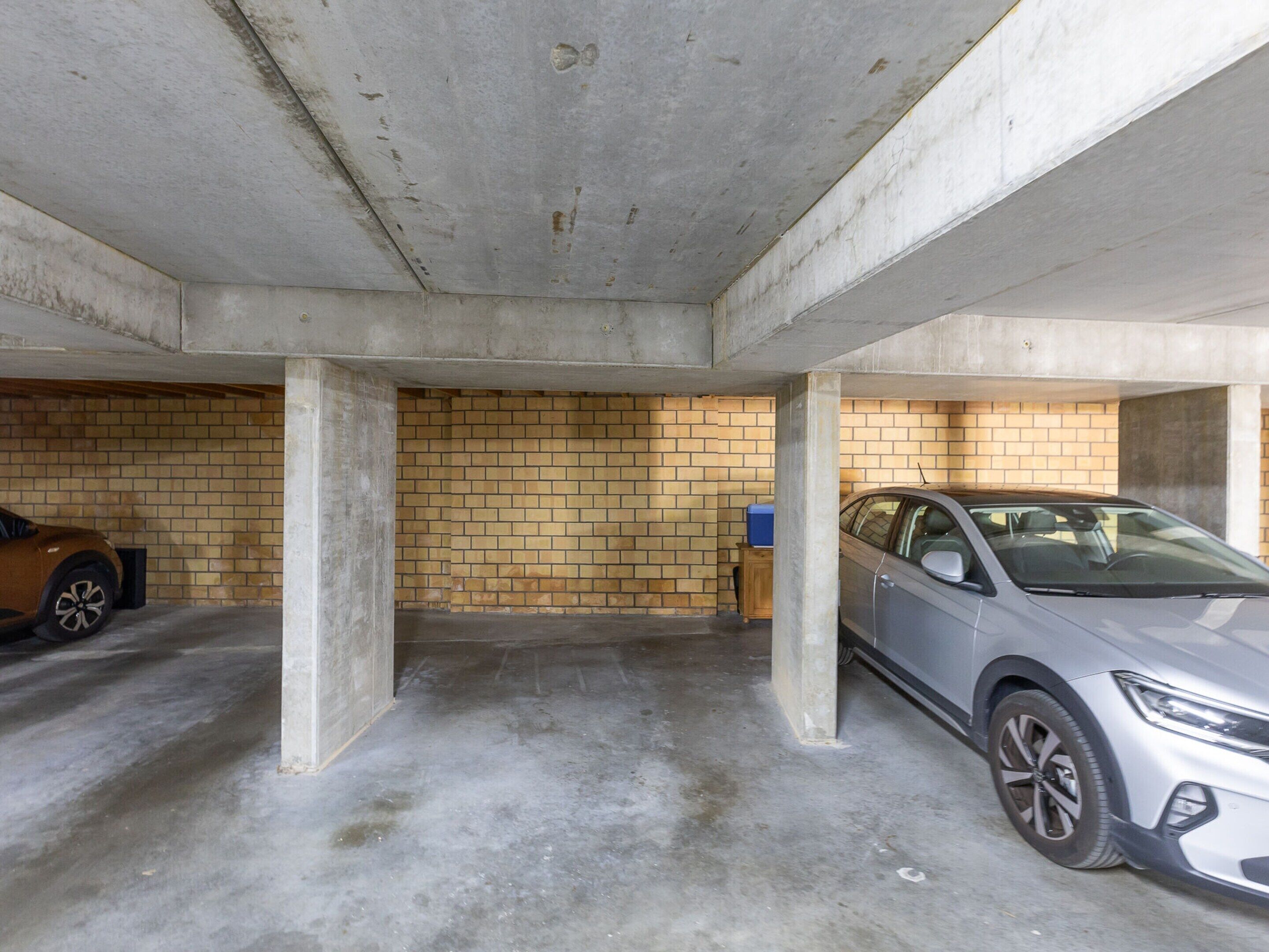 A parking garage with two cars parked, concrete pillars, and a brick wall.