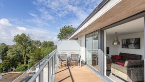 A modern house with a wooden deck, a glass door leading to a living area with a sofa and a dining table. - Bright Apartment With Sunny Terrace (Middelkerke)